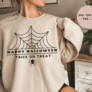 K&ouml;nnte beinhalten: Ein beiger Pullover mit einem schwarzen Spinnennetz-Design und dem Text "Happy Halloween Trick or Treat".