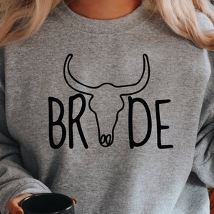 May include: Gray sweatshirt with a black outline of a bull skull and the word "BRIDE" written in a stylized font.