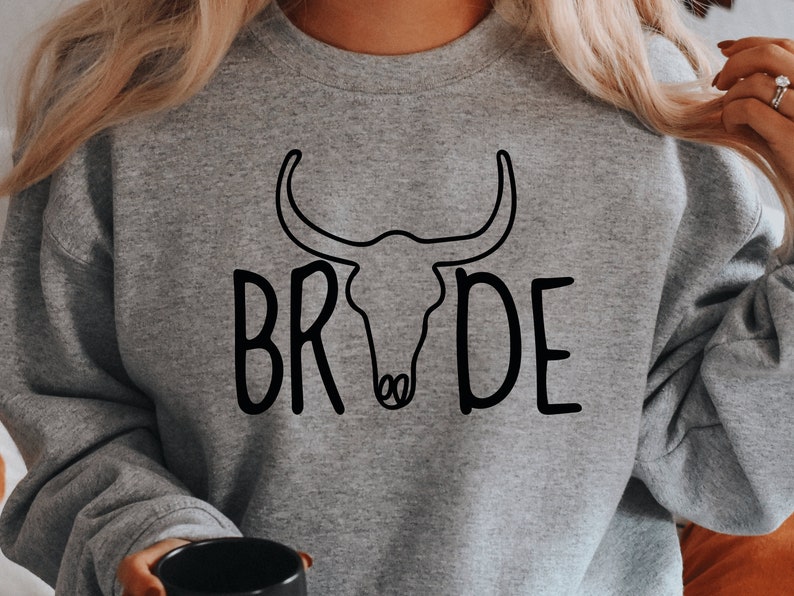 May include: Gray sweatshirt with a black outline of a bull skull and the word "BRIDE" written in a stylized font.