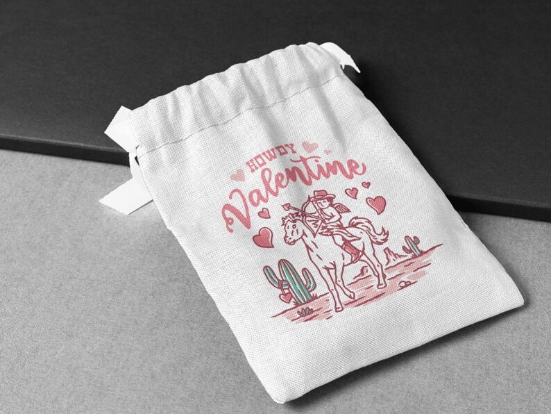 May include: White drawstring bag with a pink and white illustration of a cowgirl riding a horse with the text "Howdy Valentine" and pink hearts.