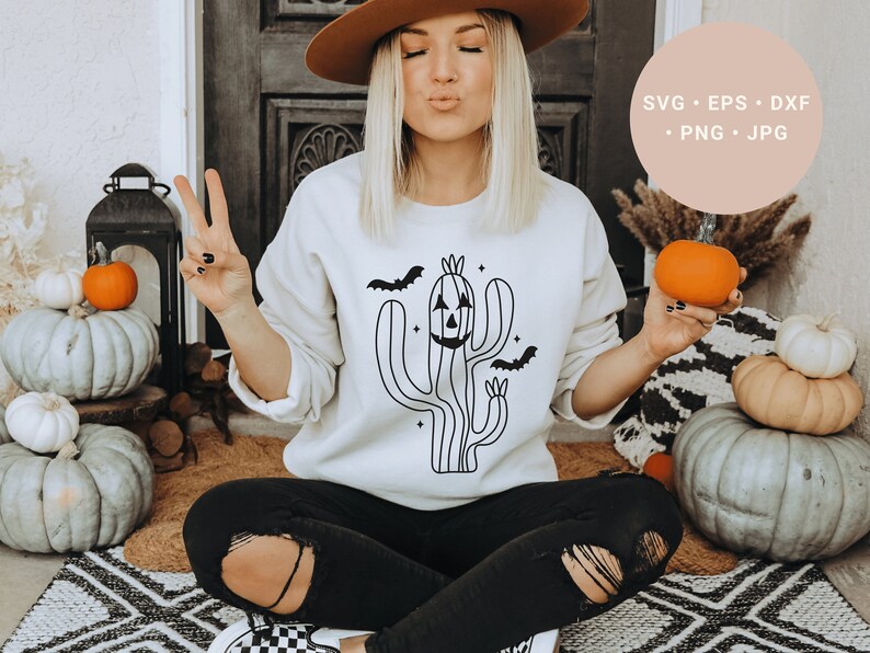 May include: A white sweatshirt featuring a black line drawing of a cactus with a jack-o'-lantern face and bats flying around it. The text "SVG - EPS - DXF - PNG - JPG" is in a peach-coloured circle in the top right corner of the image.