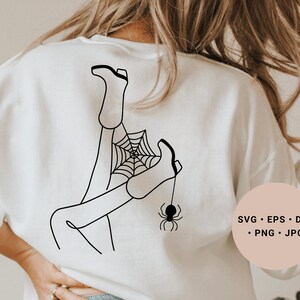 May include: A white sweatshirt with a black line drawing of a person's legs tangled in a spider web with a spider hanging from the web. The text "SVG - EPS - DXF - PNG - JPG" is on a pink circle in the lower right corner of the image.