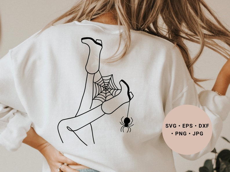 May include: A white sweatshirt with a black line drawing of a person's legs tangled in a spider web with a spider hanging from the web. The text "SVG - EPS - DXF - PNG - JPG" is on a pink circle in the lower right corner of the image.