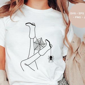 May include: A white t-shirt with a black line drawing of a person's legs tangled in a spider web with a spider hanging from the web.