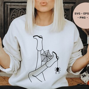 May include: A white sweatshirt with a black line drawing of a woman's legs in boots tangled in a spider web with a spider hanging from the web.