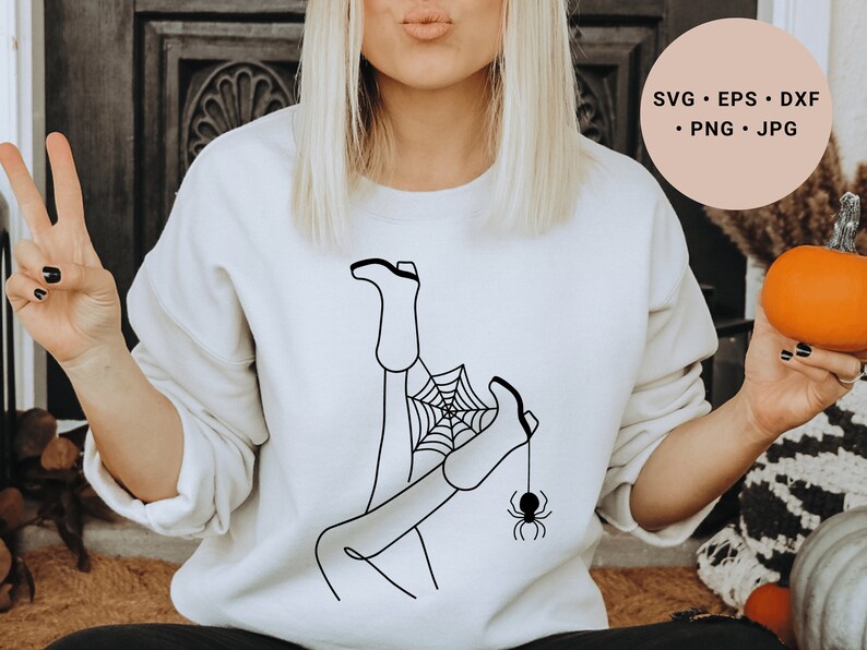 May include: A white sweatshirt with a black line drawing of a woman's legs in boots tangled in a spider web with a spider hanging from the web.