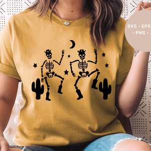 May include: A yellow t-shirt with a design of two skeletons wearing cowboy hats and boots, dancing with cacti on either side. The skeletons are black and the cacti are black against a yellow background.