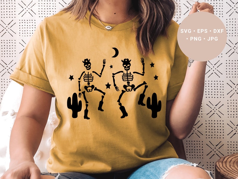 May include: A yellow t-shirt with a design of two skeletons wearing cowboy hats and boots, dancing with cacti on either side. The skeletons are black and the cacti are black against a yellow background.