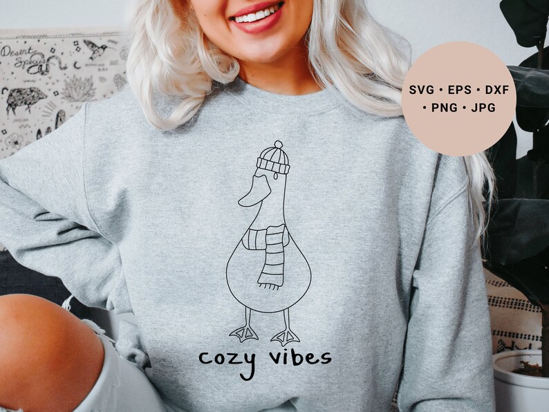 K&ouml;nnte beinhalten: Ein graues Sweatshirt mit einer schwarzen Strichzeichnung eines Entchens, das einen Hut und einen Schal tr&auml;gt. Der Text "cozy vibes" ist unter dem Entchen gedruckt.