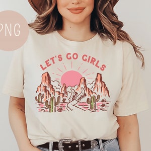 May include: A white t-shirt with a graphic design of a desert landscape with a pink sunset, cacti, and the text "Let's Go Girls".
