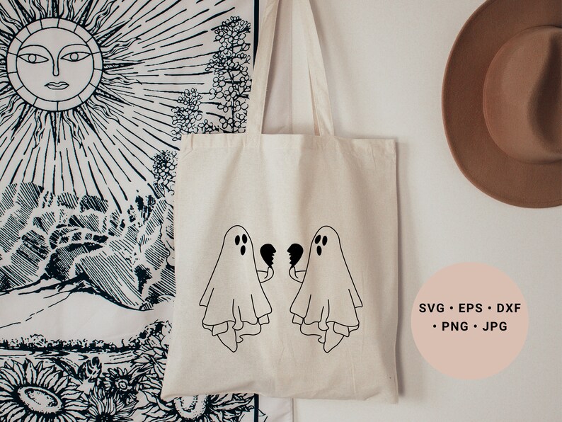May include: A white tote bag featuring two black ghosts holding broken hearts. The bag is hanging on a white wall with a black and white tapestry and a brown hat in the background. The text "SVG - EPS - DXF - PNG - JPG" is printed on a pink circle in the bottom right corner of the image.