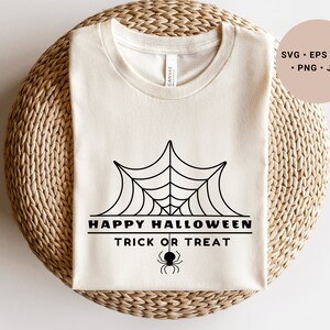 K&ouml;nnte beinhalten: Ein wei&szlig;es T-Shirt mit einem schwarzen Spinnennetz-Design und dem Text "Happy Halloween Trick or Treat".
