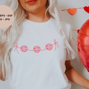 May include: A white t-shirt with a pink disco ball garland design. The design features four disco balls connected by a string with pink bows on each end.