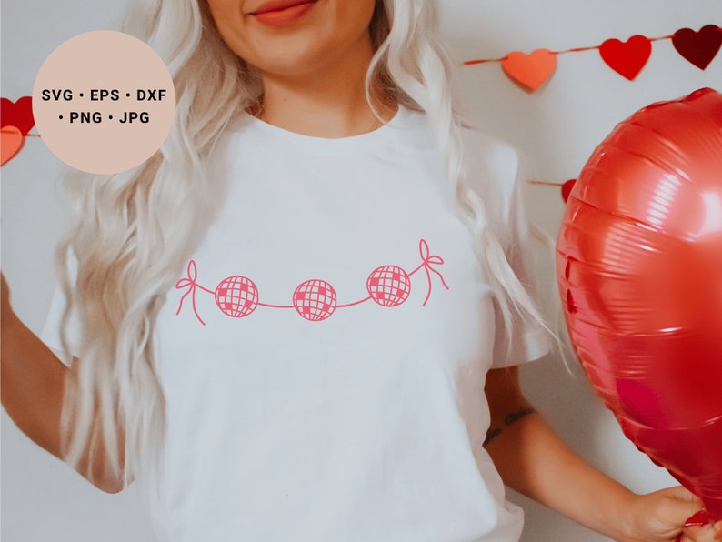 May include: A white t-shirt with a pink disco ball garland design. The design features four disco balls connected by a string with pink bows on each end.