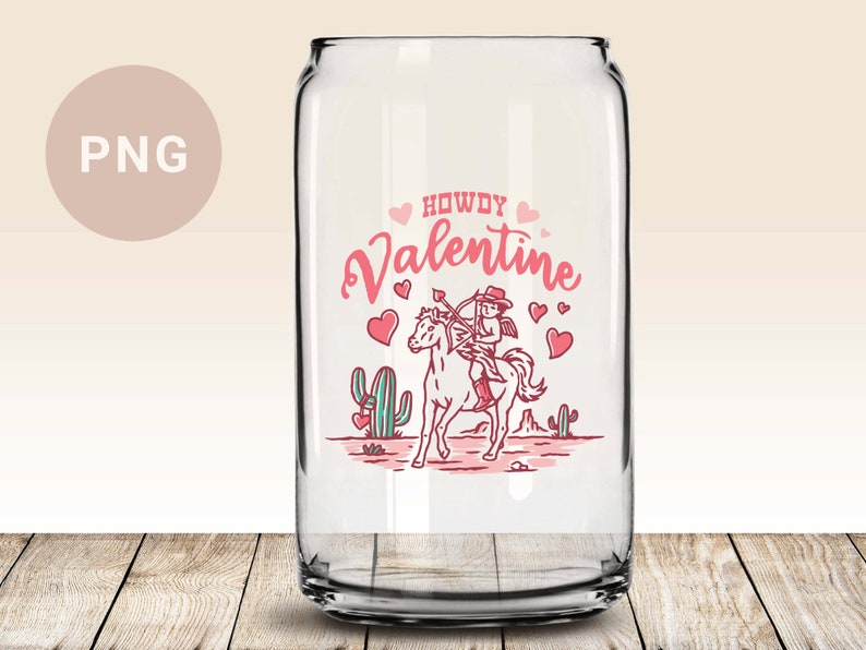 May include: A clear glass can with a pink and red design featuring a cowboy cupid riding a horse with the text "Howdy Valentine".
