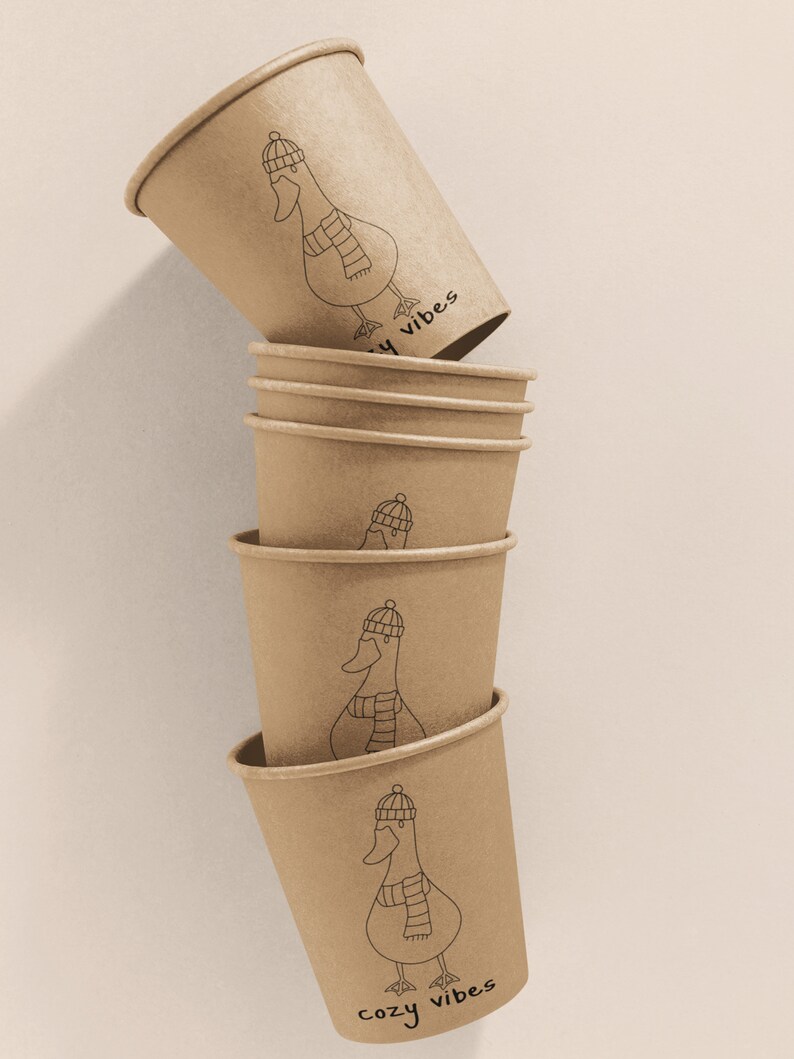 K&ouml;nnte beinhalten: Stapel aus sechs braunen Pappbechern mit einer Schwarzwei&szlig;illustration einer Gans, die einen Hut und einen Schal tr&auml;gt. Der Text "cozy vibes" ist auf dem untersten Becher aufgedruckt.