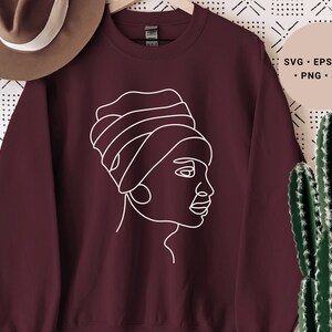 Könnte beinhalten: Burgunderfarbener Pullover mit einer weißen Linienzeichnung eines Frauenkopfes mit Kopftuch.