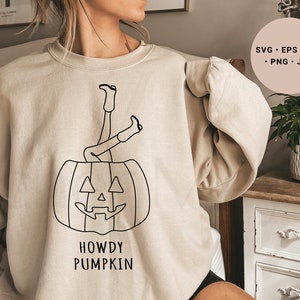 May include: A beige sweatshirt with a black line drawing of a person's legs sticking out of a pumpkin. The text "Howdy Pumpkin" is printed below the pumpkin.