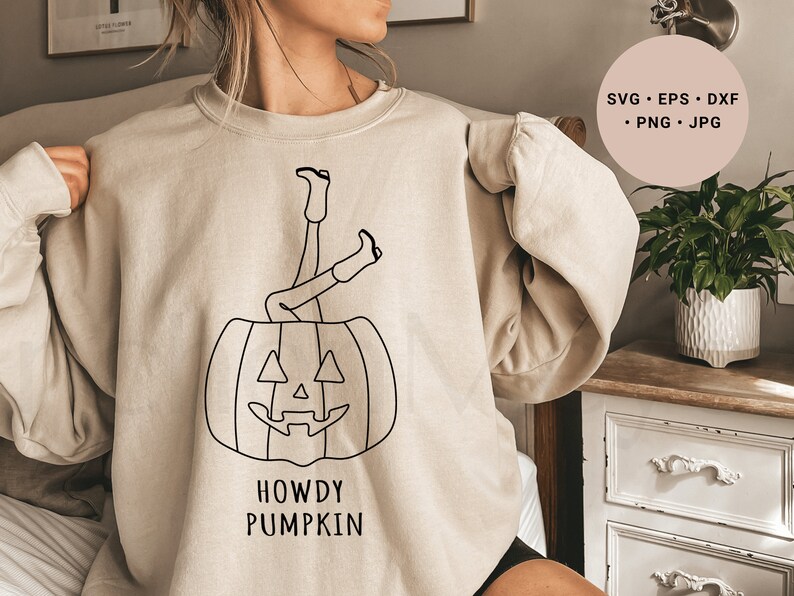 May include: A beige sweatshirt with a black line drawing of a person's legs sticking out of a pumpkin. The text "Howdy Pumpkin" is printed below the pumpkin.