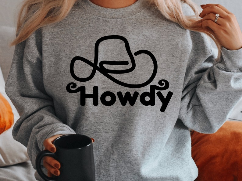 Może przedstawiać: Szara bluza z czarnym konturem kowbojskiego kapelusza i nadrukiem słowa "Howdy" z przodu.