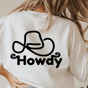 Może przedstawiać: Biała bluza z czarnym rysunkiem kowbojskiego kapelusza i napisem "Howdy" pod spodem.