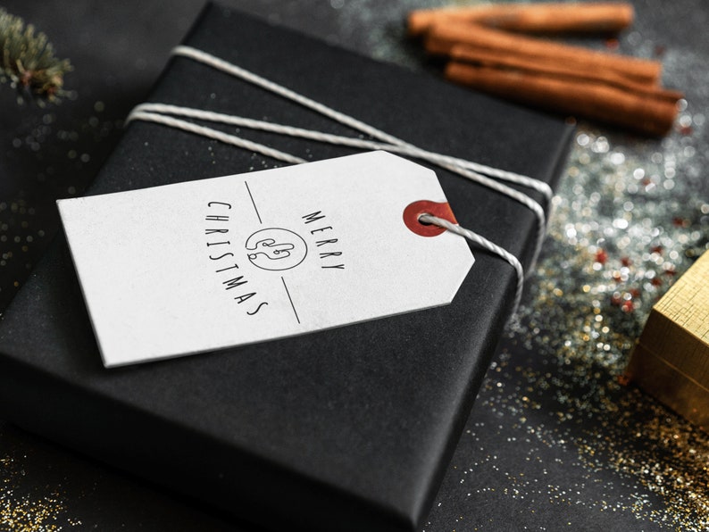 May include: A white gift tag with black text that reads "Merry Christmas" and a simple illustration of a Christmas tree. The tag is tied to a black gift box with white twine.