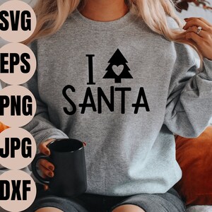 Könnte beinhalten: Ein graues Sweatshirt mit dem Text "I love Santa" und einer schwarzen Silhouette eines Weihnachtsbaums mit einem Herzen darin.