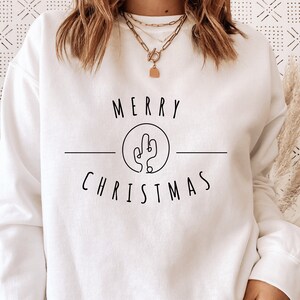 May include: White sweatshirt with a black graphic design that says "Merry Christmas" with a cactus illustration inside a circle.
