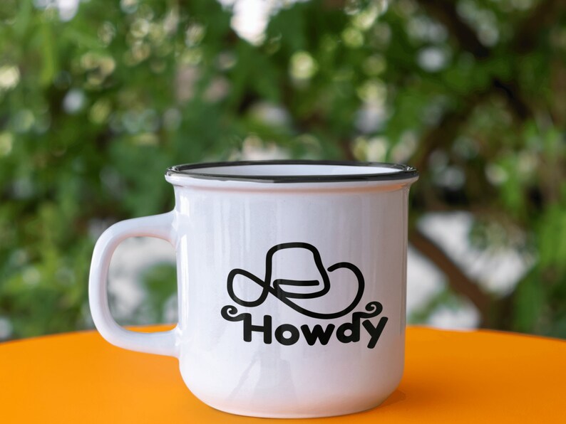 Może przedstawiać: Biały kubek ceramiczny z czarną obw&oacute;dką i czarnym wzorem w postaci kowbojskiego kapelusza z napisem "Howdy" pod spodem.