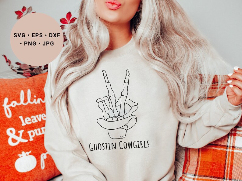 May include: A white sweatshirt with a black line drawing of a skeleton hand making a peace sign. The text "Ghostin Cowgirls" is printed below the hand.