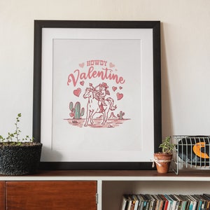 May include: A framed print with a pink and white illustration of a cowboy riding a horse with the text "Howdy Valentine" and hearts.