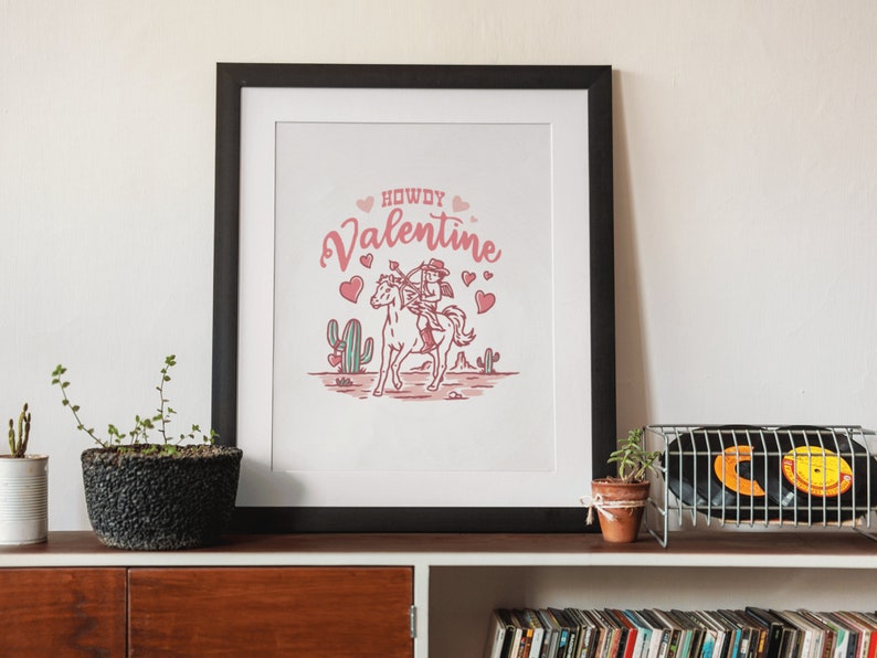 May include: A framed print with a pink and white illustration of a cowboy riding a horse with the text "Howdy Valentine" and hearts.