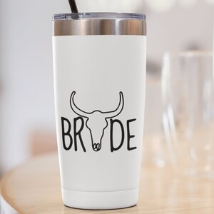 May include: White stainless steel tumbler with a black bull skull and the word "BRIDE" printed on it. The tumbler has a black straw.