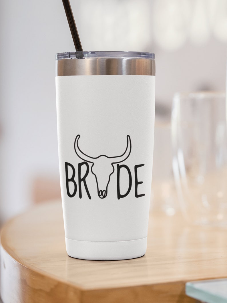 May include: White stainless steel tumbler with a black bull skull and the word "BRIDE" printed on it. The tumbler has a black straw.