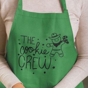 May include: Green apron with the text "THE cookie CREW" and a gingerbread man wearing a cowboy hat and holding a candy cane.