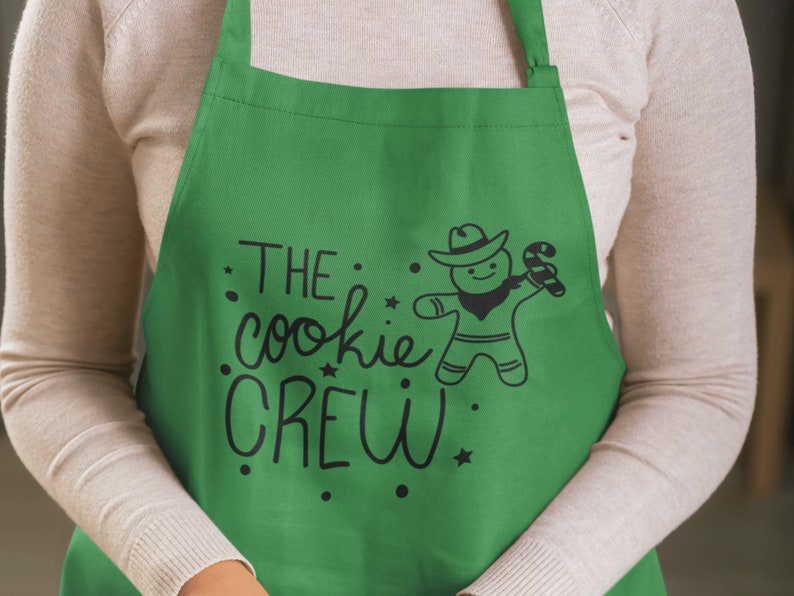 May include: Green apron with the text "THE cookie CREW" and a gingerbread man wearing a cowboy hat and holding a candy cane.