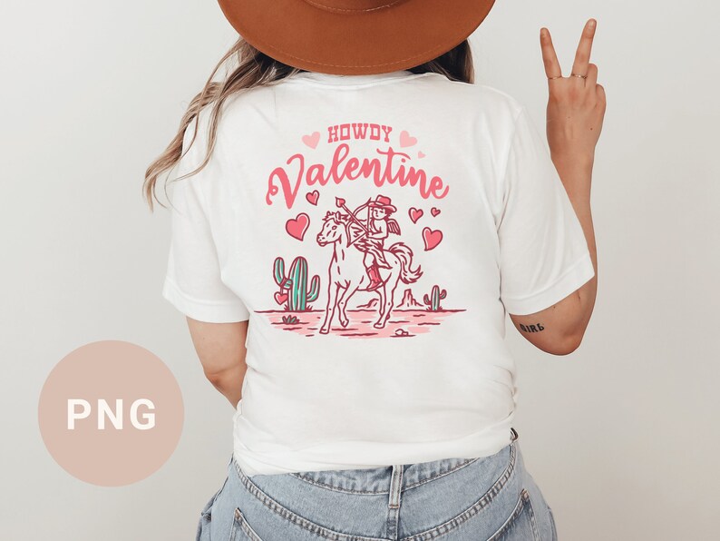 May include: White t-shirt with a pink and red graphic of a cowboy riding a horse with the text "Howdy Valentine".