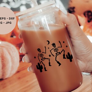 May include: A clear glass tumbler with a brown beverage inside. The tumbler has a black design of two skeletons dancing with a cactus and stars. The text "SVG. EPS. DXF. PNG. JPG" is visible in the background.