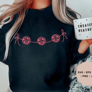 May include: A black sweatshirt with a pink design of a string of disco balls with the text "Sweater Weather" on a white mug.