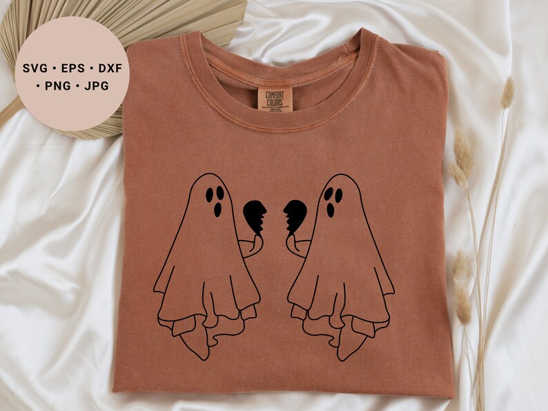 May include: A brown t-shirt featuring a black graphic of two ghosts holding broken heart halves. The ghosts are facing each other and have three dots for eyes.