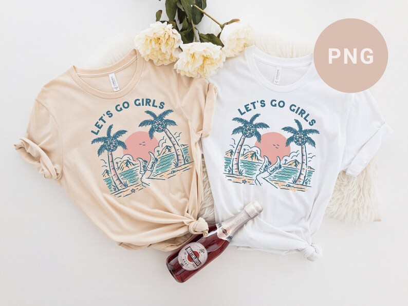 K&ouml;nnte beinhalten: Zwei T-Shirts, eines beige und eines wei&szlig;, jeweils mit einer Strandmotiv-Grafik. Das Design umfasst Palmen, einen Sonnenuntergang und den Text "LET'S GO GIRLS" in kreisf&ouml;rmiger Anordnung. Eine Flasche Sekt befindet sich im Vordergrund.