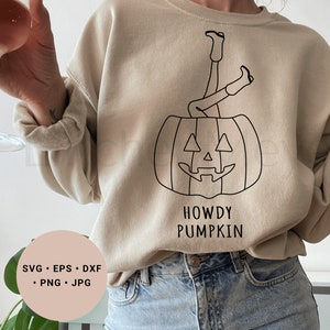 May include: A beige sweatshirt with a black line drawing of a person with their legs sticking out of a jack-o'-lantern. The text "Howdy Pumpkin" is printed below the image.