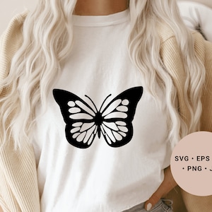 Könnte beinhalten: Ein weißes T-Shirt mit einem schwarzen Schmetterlingsmotiv. Der Schmetterling hat ein detailliertes Design mit filigranen Flügeln. Das Shirt ist ein beliebtes Design zum Basteln und Erstellen von individueller Kleidung.