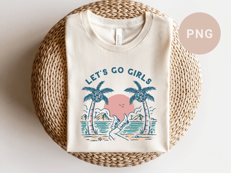 K&ouml;nnte beinhalten: Cremefarbenes T-Shirt mit Strandmotiv. Das Design zeigt Palmen, eine rosa Sonne und den Text "LET'S GO GIRLS" in Blau. Das Shirt liegt gefaltet auf einer gewebten, kreisf&ouml;rmigen Oberfl&auml;che.