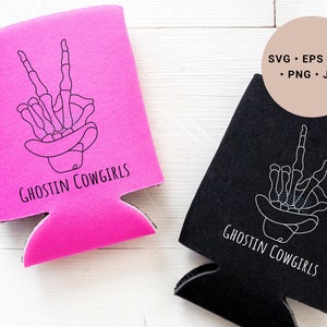May include: Two black and pink can coolers with a skeleton hand making the peace sign wearing a cowboy hat. The text on the coolers says "Ghostin Cowgirls".