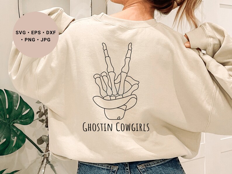 May include: A cream-colored sweatshirt with a black line drawing of a skeleton hand making a peace sign. The text "Ghostin Cowgirls" is printed below the hand.