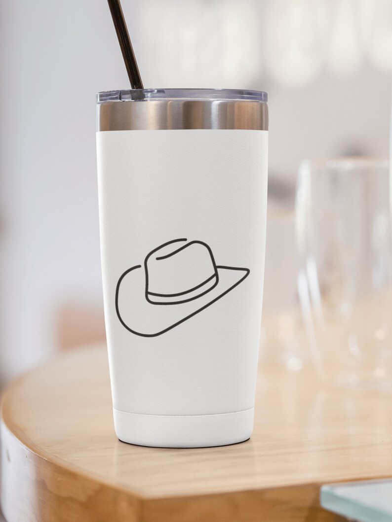 May include: White stainless steel tumbler with a black line drawing of a cowboy hat on the side. The tumbler has a black lid and a black straw.