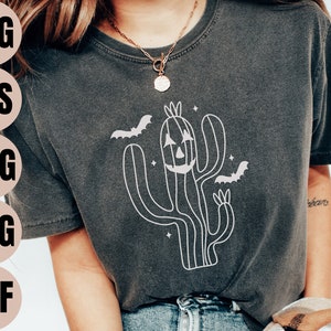 May include: A dark grey t-shirt featuring a white outline of a cactus with a jack-o'-lantern face and bats flying around it.