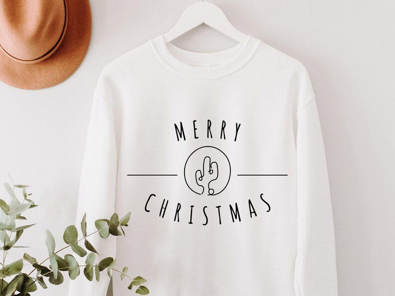 May include: White sweatshirt with black text that reads "Merry Christmas" with a cactus graphic in a circle.