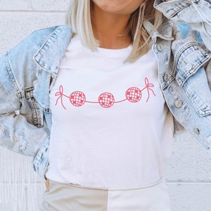 May include: White t-shirt with a pink graphic of a string of disco balls.